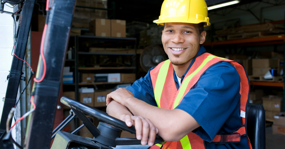 Photo of a man in a construction vest and hard hat sitting in a vehicle and smiling at the camera.